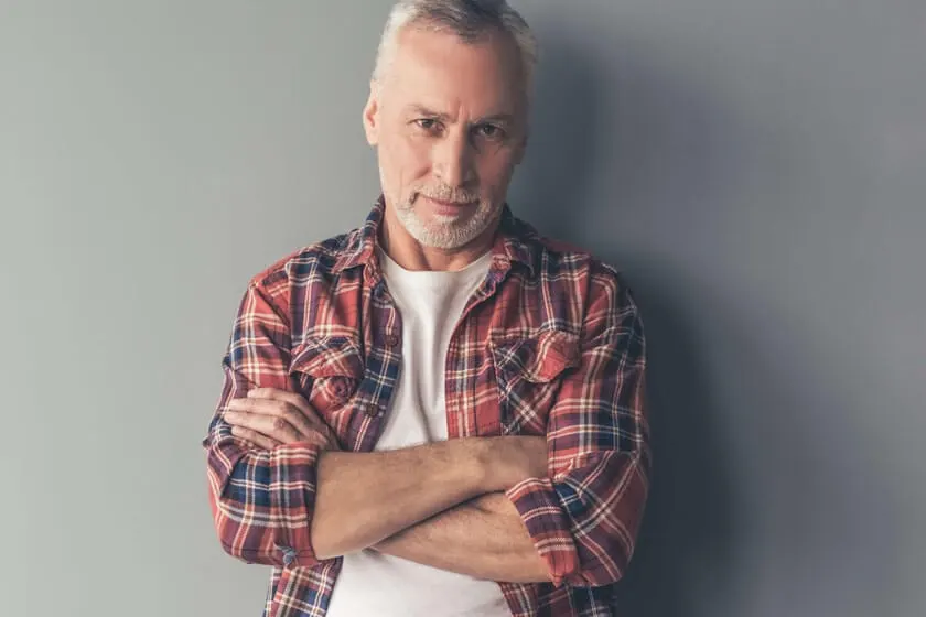Gray-haired man in a plaid shirt standing with arms crossed