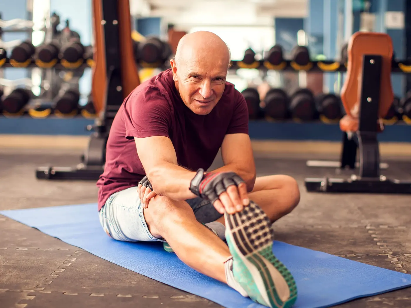 Older man stretching his hamstrings on a mat in a gym