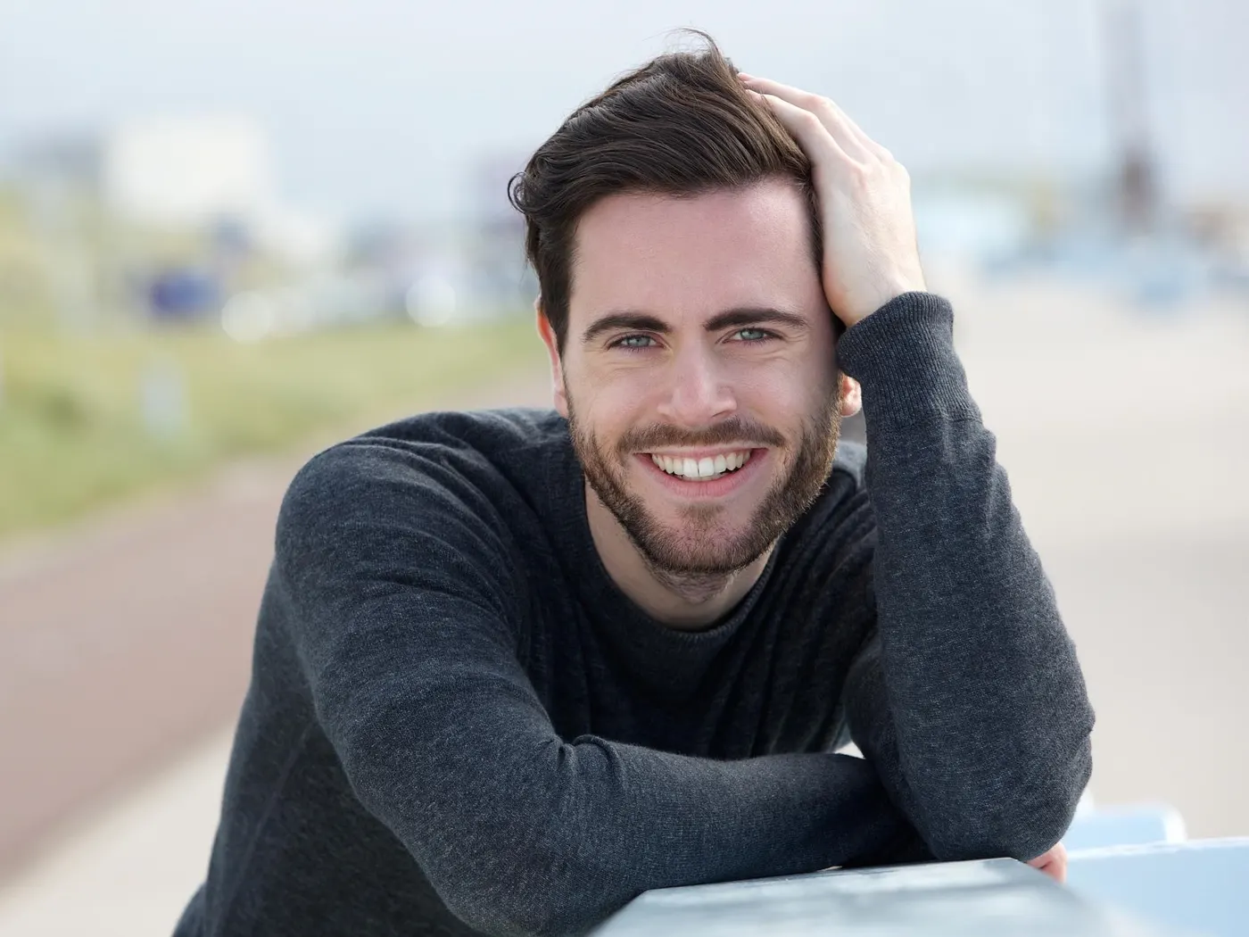 Smiling man with full dark hair resting a hand on his head