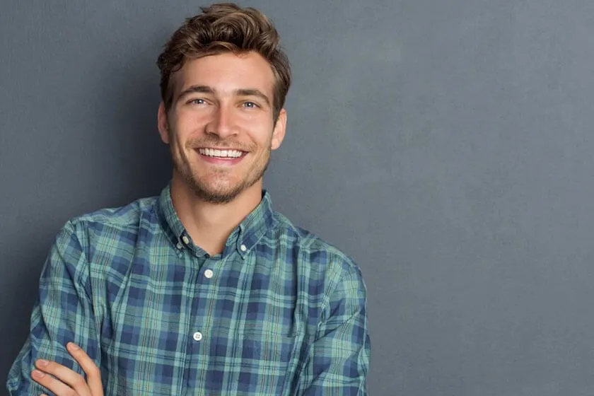 Smiling young man in a plaid shirt against a gray wall