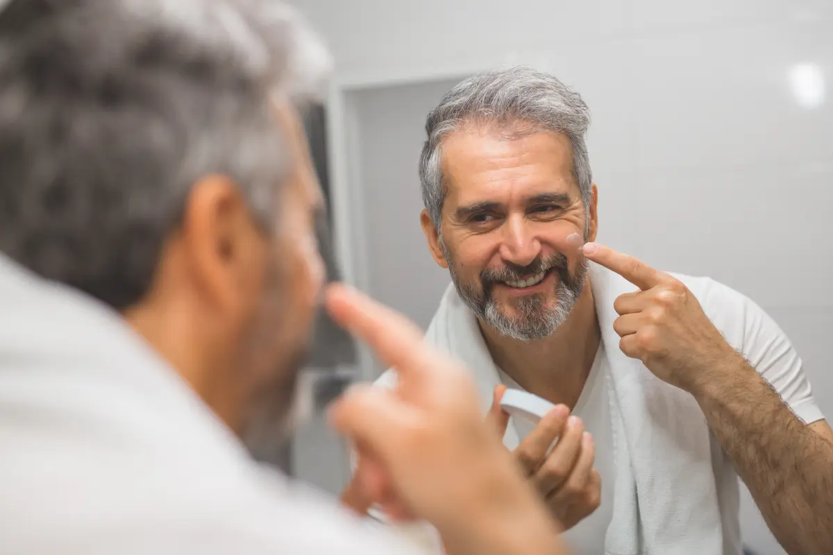 Gray-bearded man checking his face in a bathroom mirror