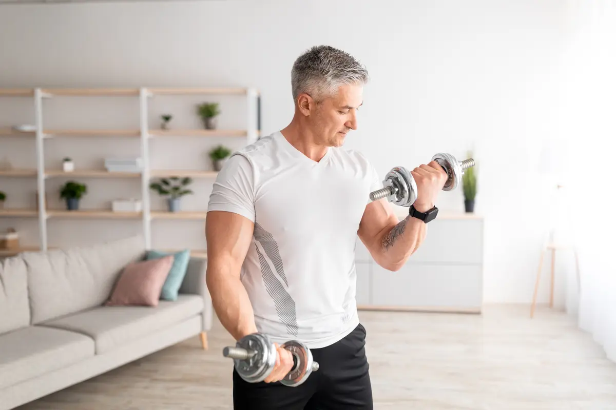Gray-haired man doing dumbbell curls at home