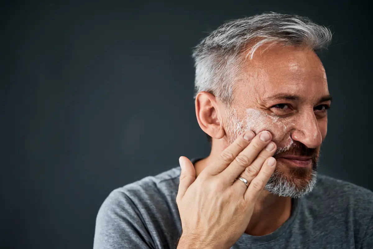 Gray-haired man putting cream on his cheek