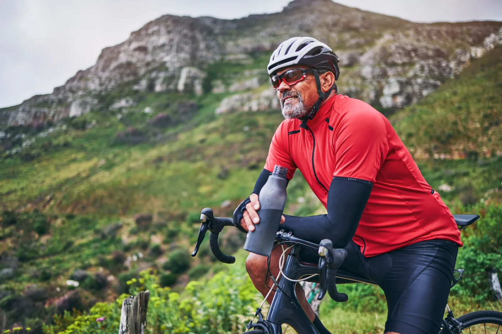 A fit man in his fifties taking a water break on his road bike in the mountains