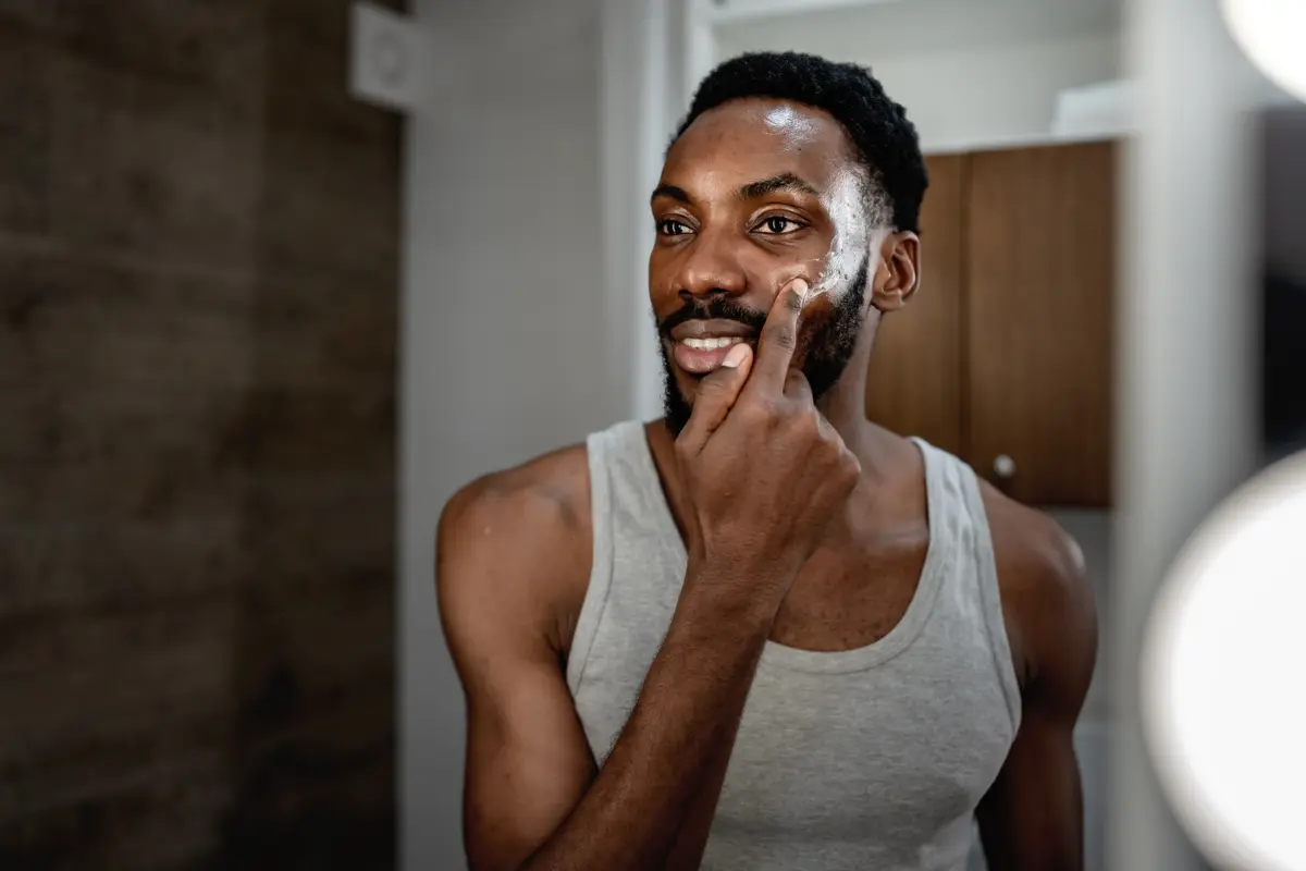 Man applying face cream in a bathroom mirror