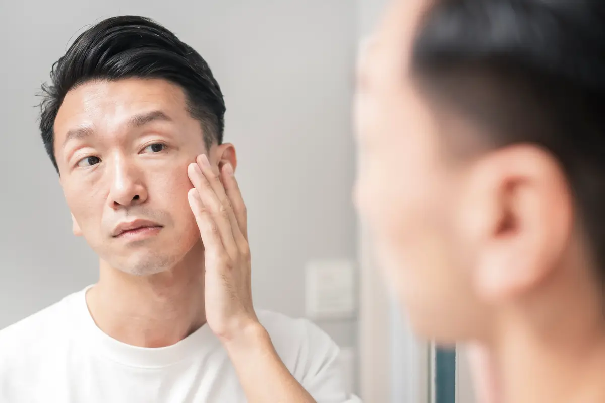 Man checking the skin on his cheek in a mirror