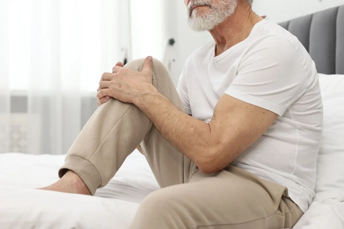 Man holding his knee while sitting on a bed