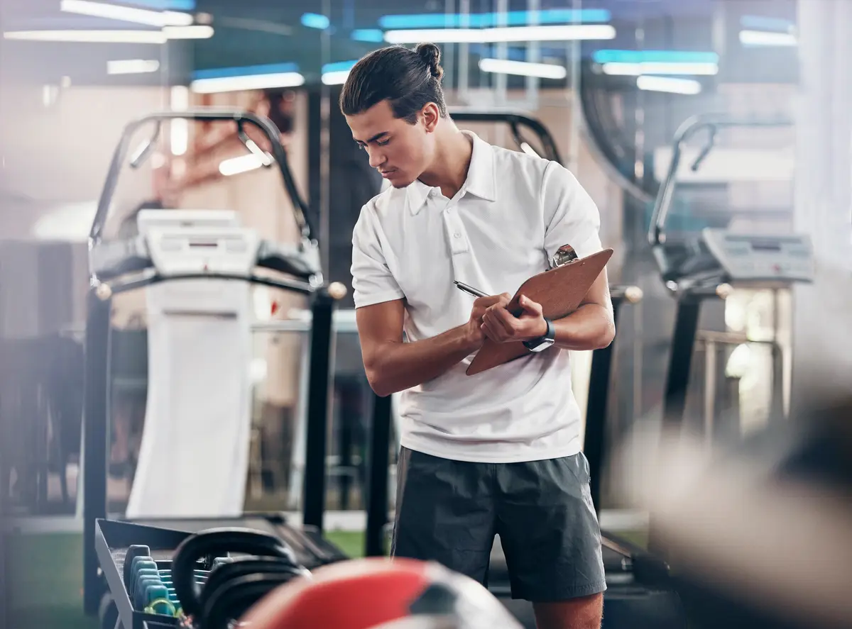Man reviewing a clipboard beside gym equipment