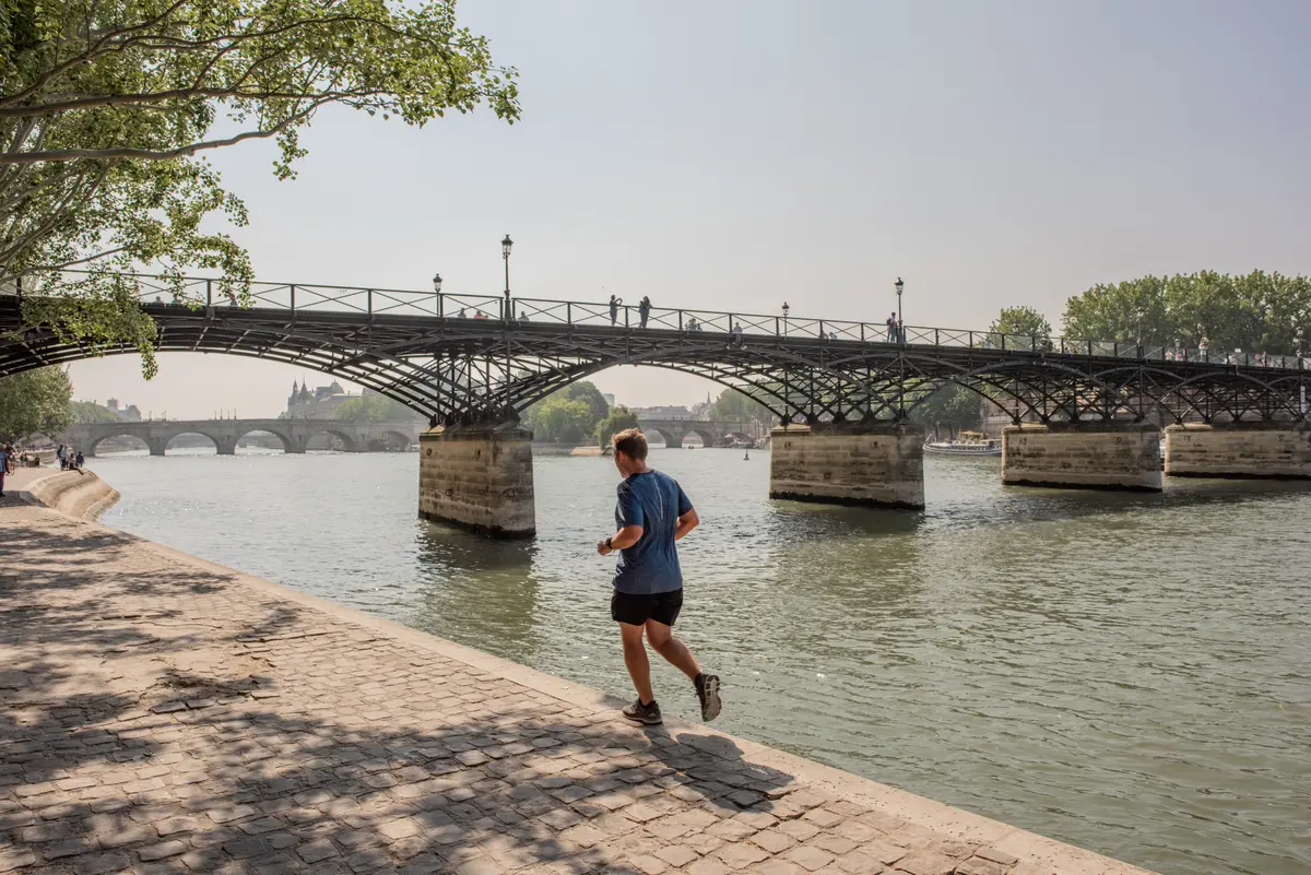 Man running along a river path under a bridge