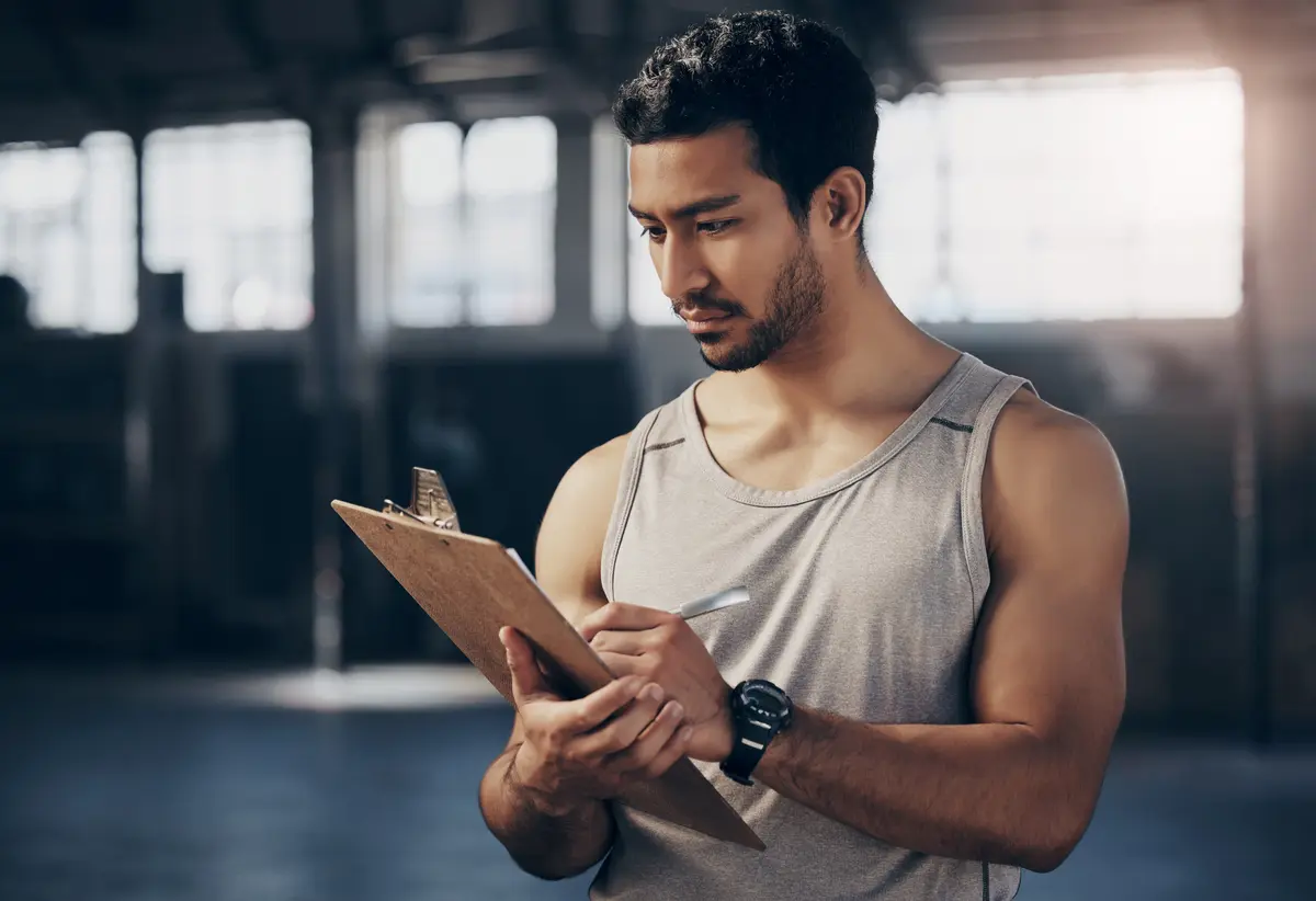 Man writing his workout log on a clipboard in the gym