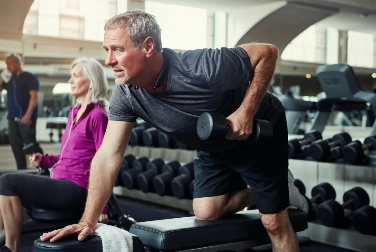 Mature man doing a dumbbell row on a gym bench
