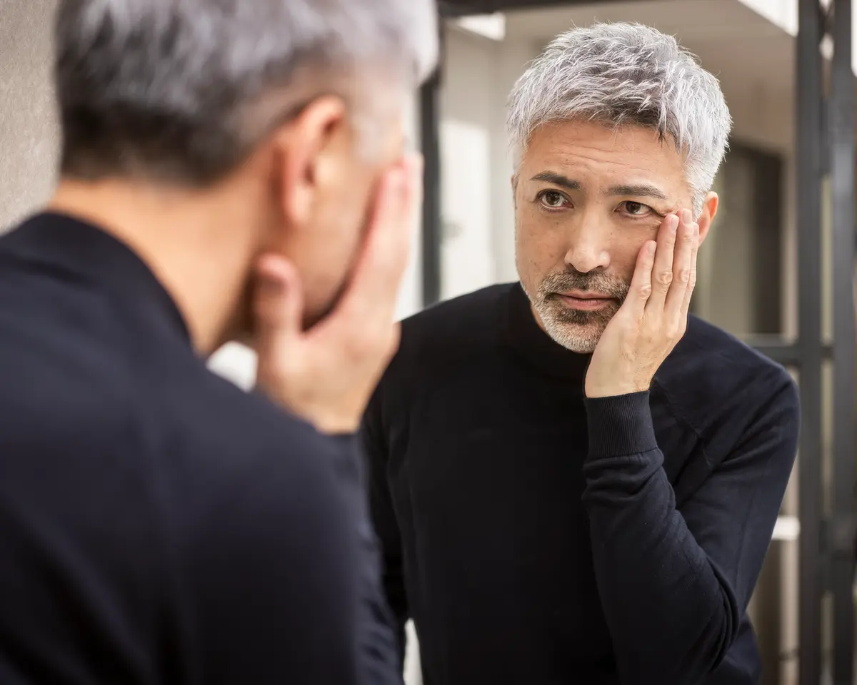 Middle-aged man checking his skin in a mirror
