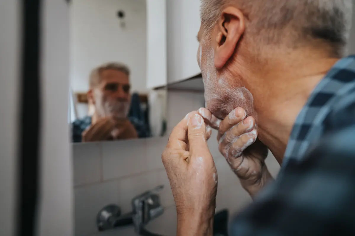 Older man examining his face in a bathroom mirror