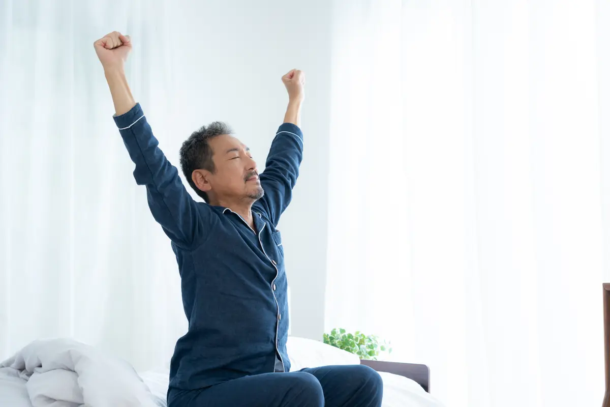 Older man stretching awake in bed in the morning