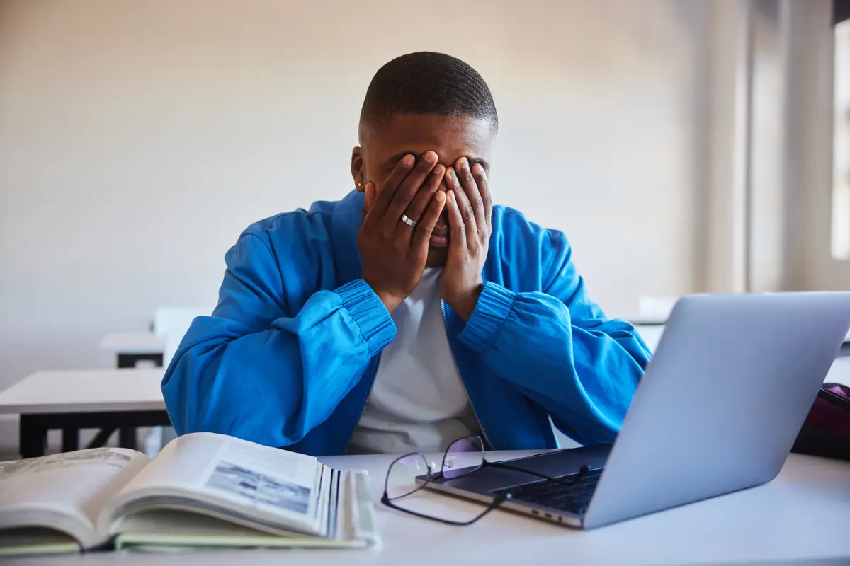 Overwhelmed man covering his face at a laptop
