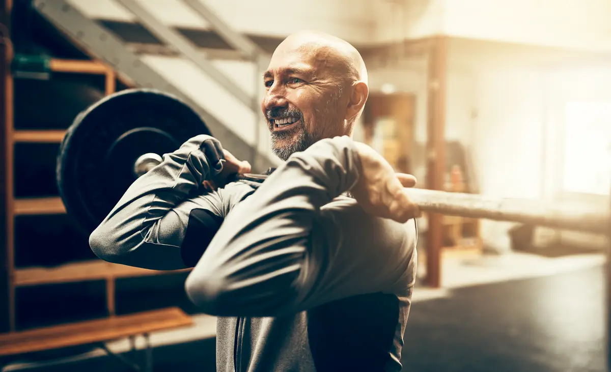 Smiling bald man lifting a barbell in a gym