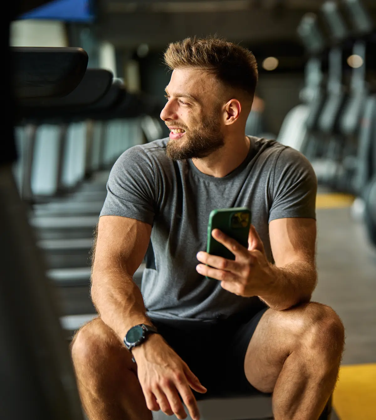 Smiling man checking his phone between gym sets