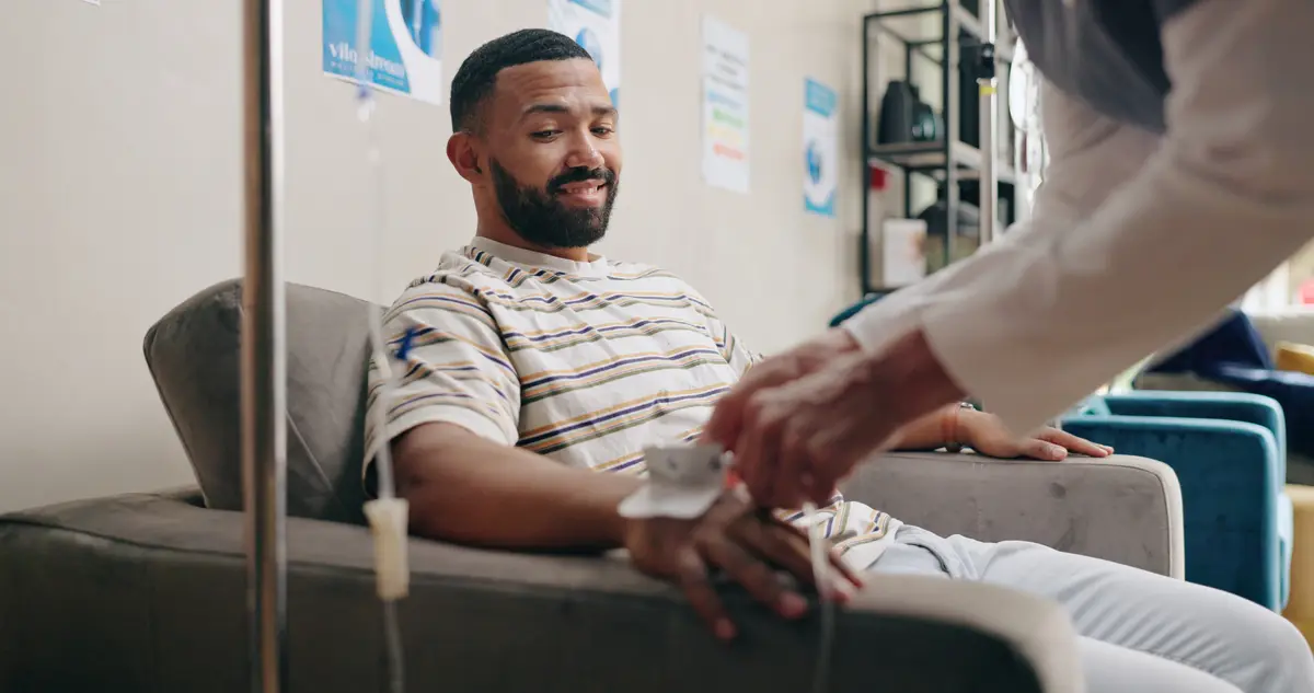Smiling man getting an IV drip from a nurse
