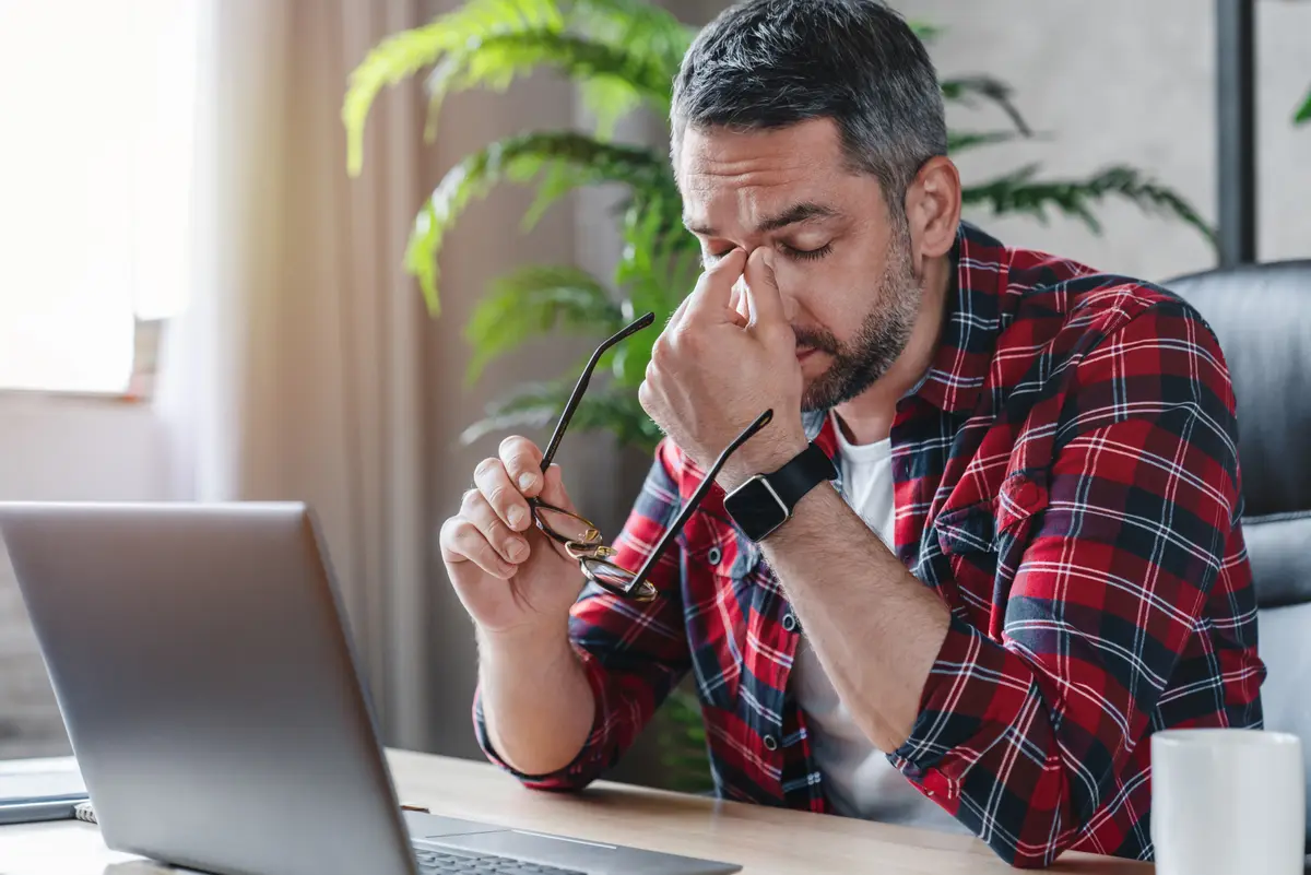 Tired man rubbing his eyes at a laptop