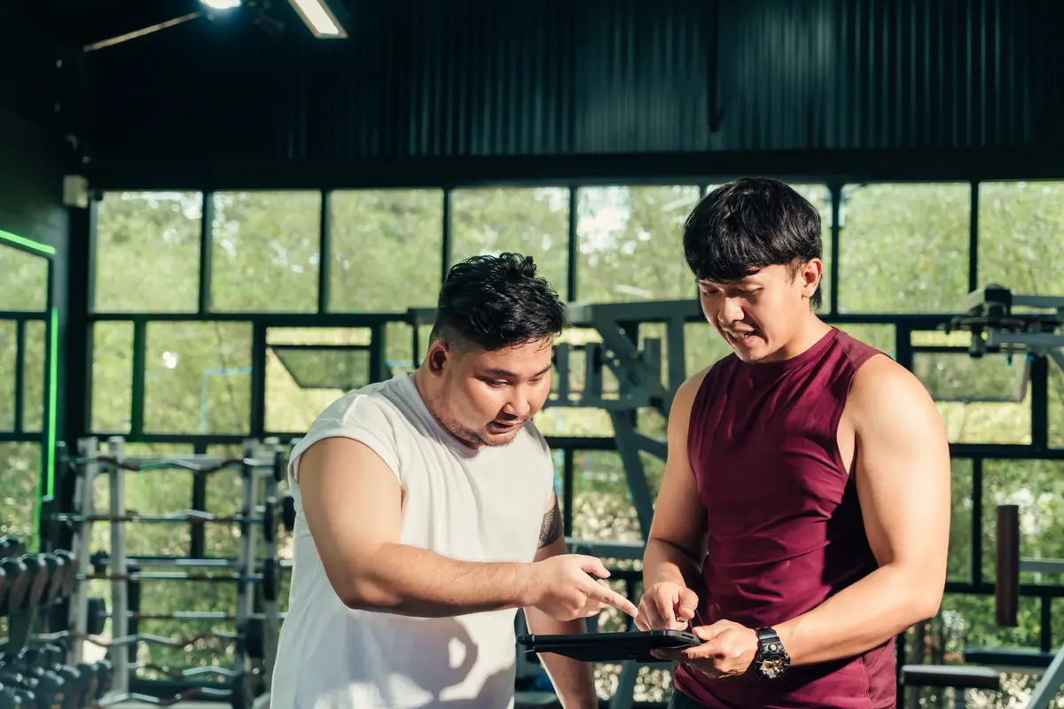 Two men reviewing a workout plan on a tablet in the gym